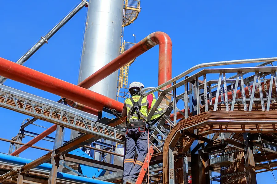 Técnico sobre a estrutura metálica de uma central de tubulação industrial